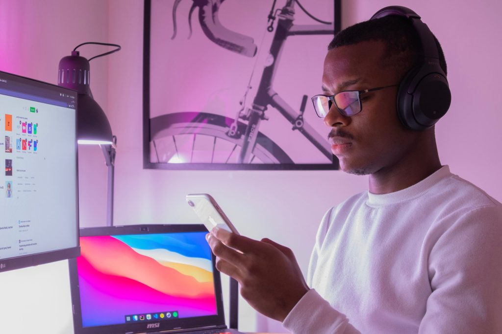 A man sits in front of his computer but is distracted by his mobile device