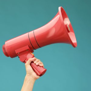 Woman holding megaphone speaker on blue background, closeup