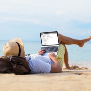 Man reading email on laptop while relaxing on beach