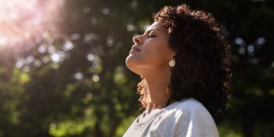 Young woman standing with her eyes closed and head raised to the sky in a park on a sunny summer afternoon