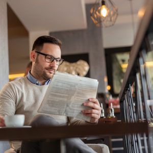Portrait of a pensive man sitting at a restaurant table, reading newspaper and drinking coffee