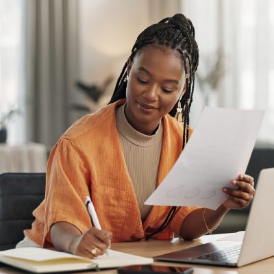 Black woman in home office, documents and laptop for research in remote work, ideas and thinking. Happy girl at desk with computer, writing notes and online search in house for freelance networking