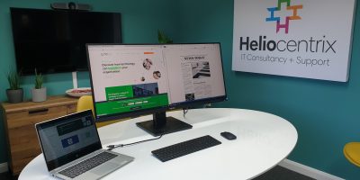 A HP X360 laptop docked with a Philips Ultrawide monitor with the Heliocentrix company logo in the background