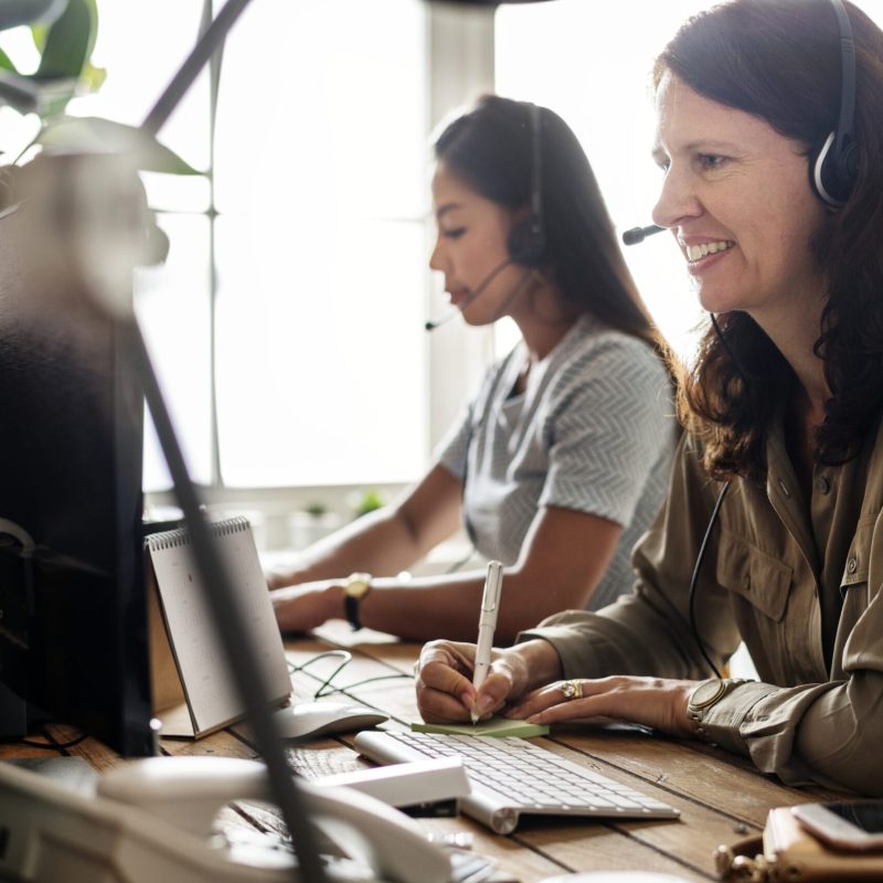 Two colleagues in a call centre, wearing headsets, providing customer service