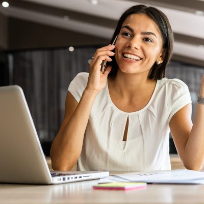 A woman at work, making a call on her mobile while using her laptop