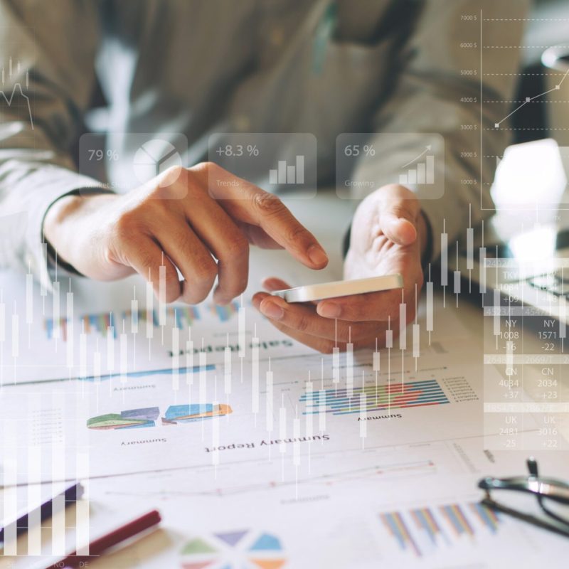 Person analysing data from paper reports while using a mobile phone to access data digitally