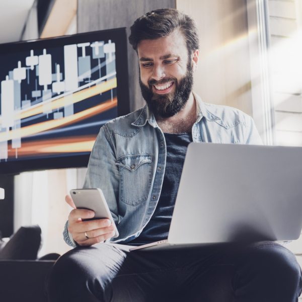 A man using a laptop and digital apps on a mobile phone, using IT systems to work efficiently.