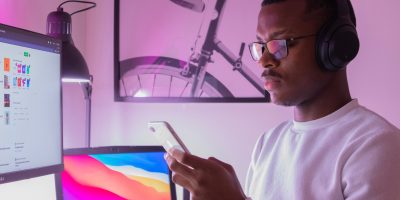 A man sits in front of his computer but is distracted by his mobile device