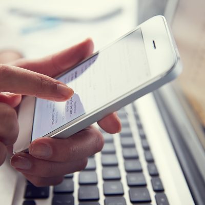 person using phone above laptop keyboard